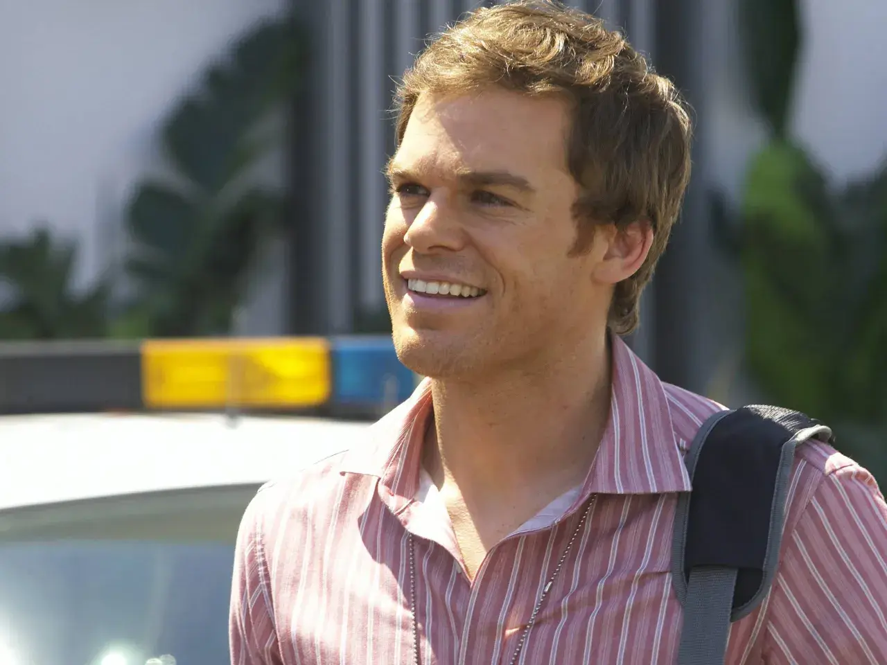 Michael C. Hall som Dexter Morgan, med en polisbil i bakgrunden.