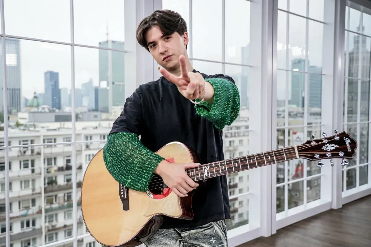 Młody muzyk z gitarą, pozdrawia gestem pokoju. Może właśnie tworzy nowe, popularne piosenki.