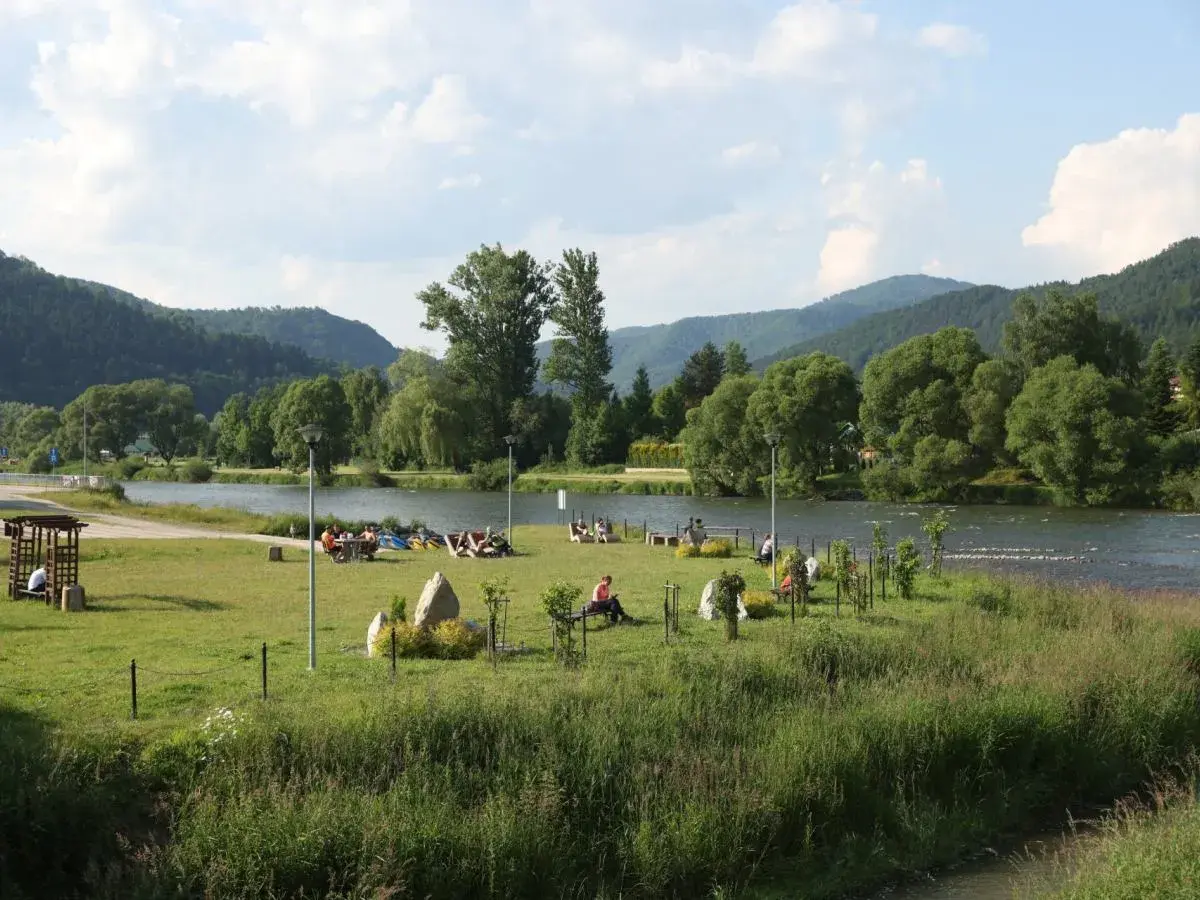 Relaks nad Dunajcem w Krościenku. Ludzie odpoczywają na trawie, w tle góry i rzeka. To świetne krościenko nad dunajcem atrakcje.