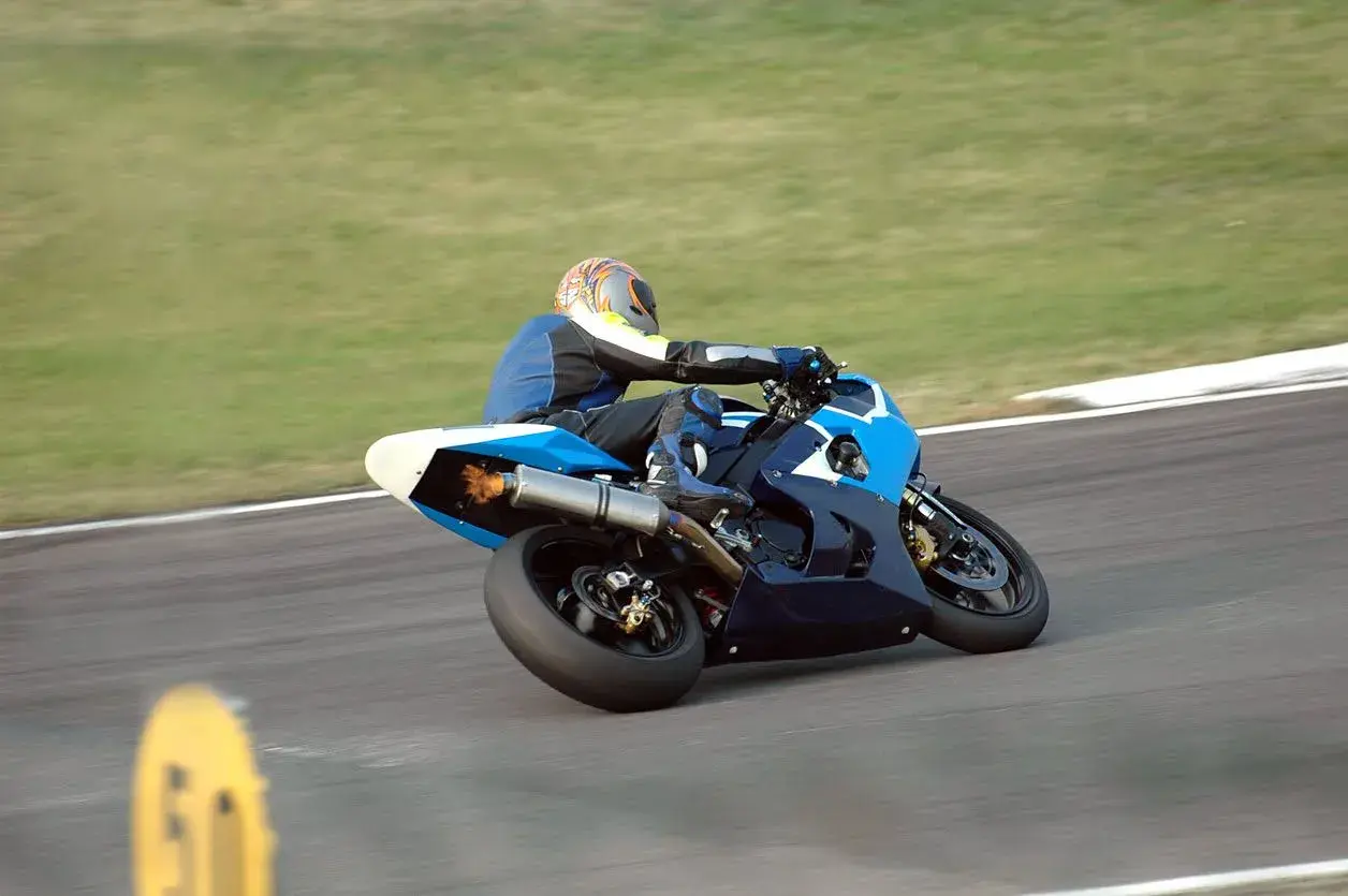 Piloto de MotoGP en plena curva, con la moto azul inclinada y llamas saliendo del escape. ¡Un auténtico holeshot!