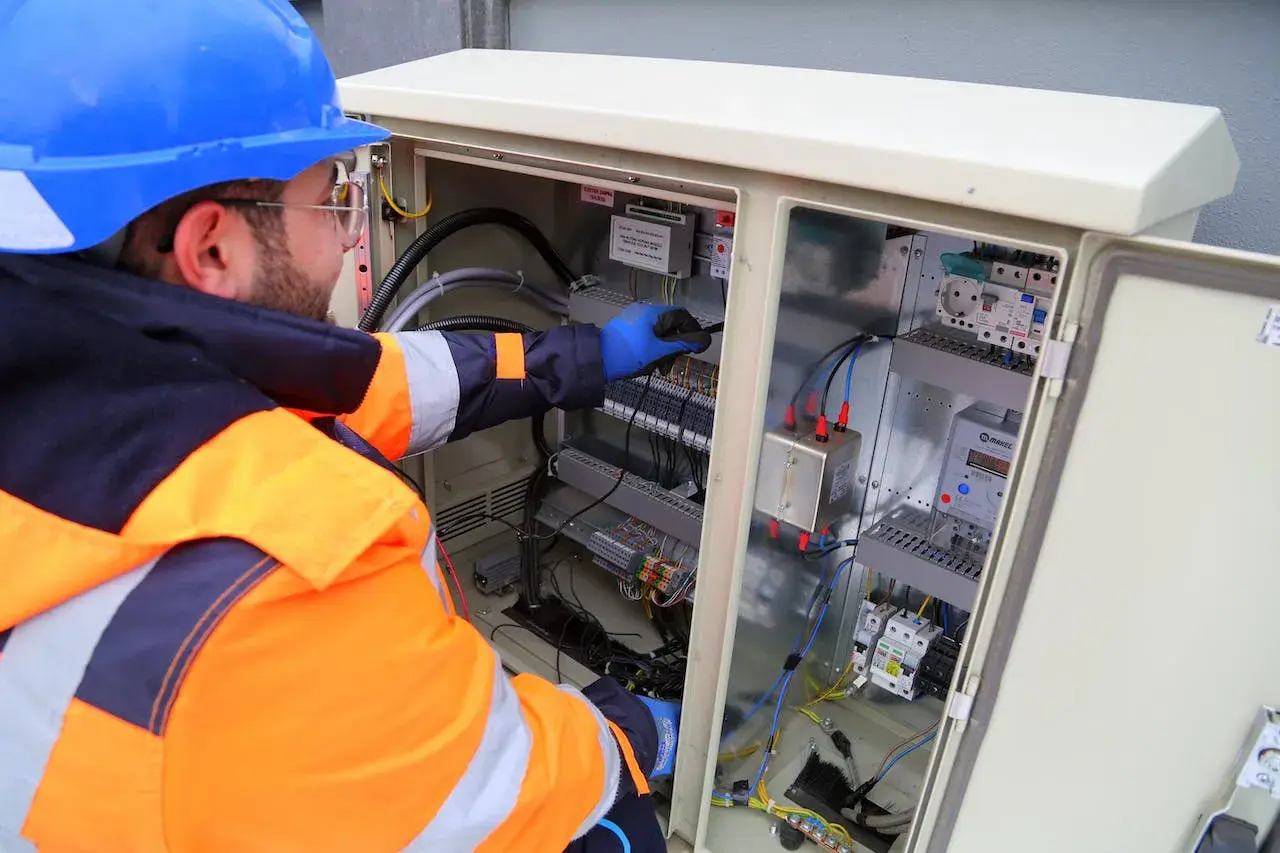 Elektryk z uprawnieniami SEP do 1kV pracuje przy rozdzielnicy elektrycznej, podłączając przewody.