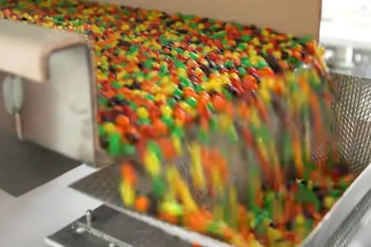 Kolorowe drażetki spadają z taśmociągu. Czy skittles są bezglutenowe? To pytanie nurtuje wielu łasuchów.
