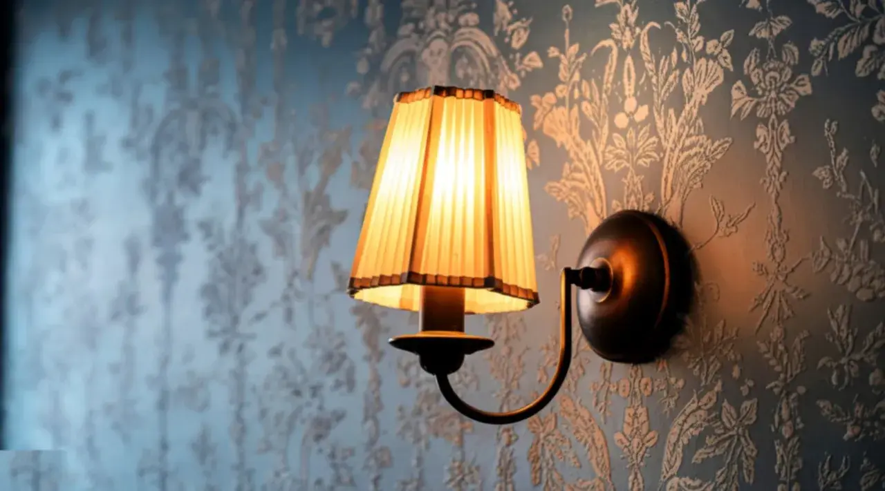 Aplique de pared rústico con pantalla plisada iluminada sobre papel tapiz floral.