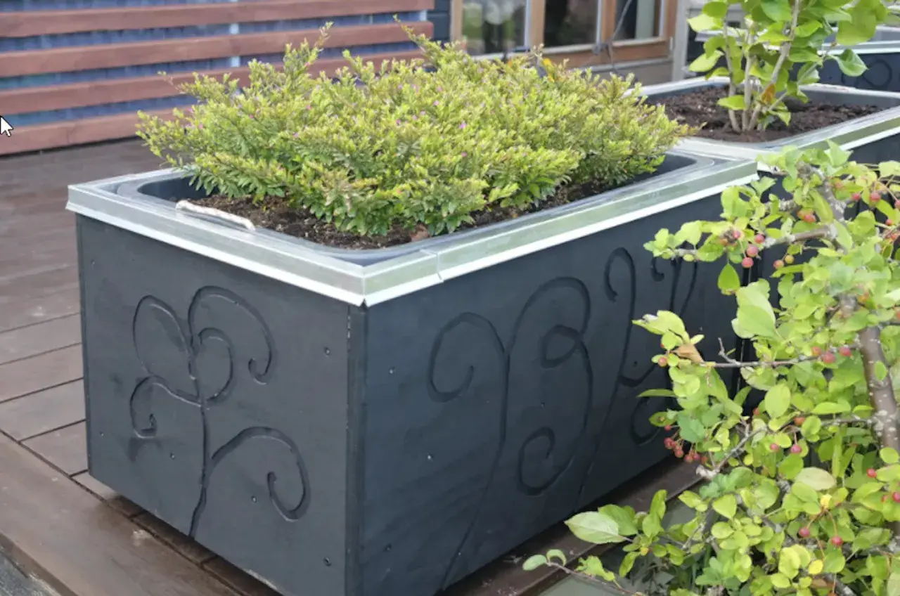 Svart blomlåda med dekorativa snirkar, perfekt för att bygga en murarbalja med grönska.