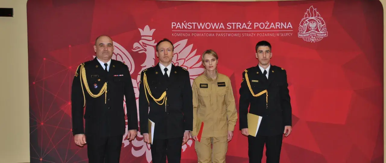 Czterech funkcjonariuszy Państwowej Straży Pożarnej w galowych mundurach i kombinezonie, z odznaczeniami i dokumentami.