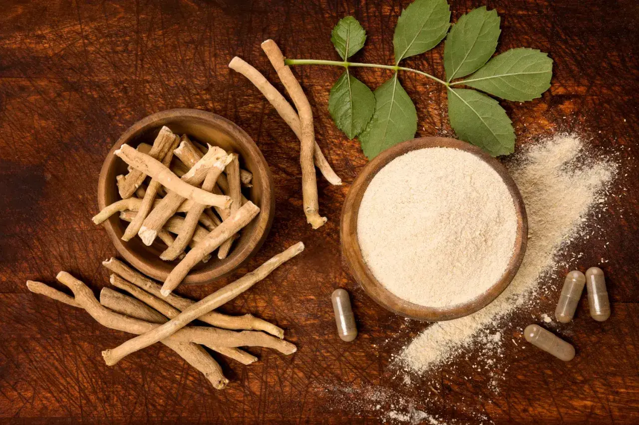 Ashwagandha roots, powder, and capsules on a wooden surface with leaves.