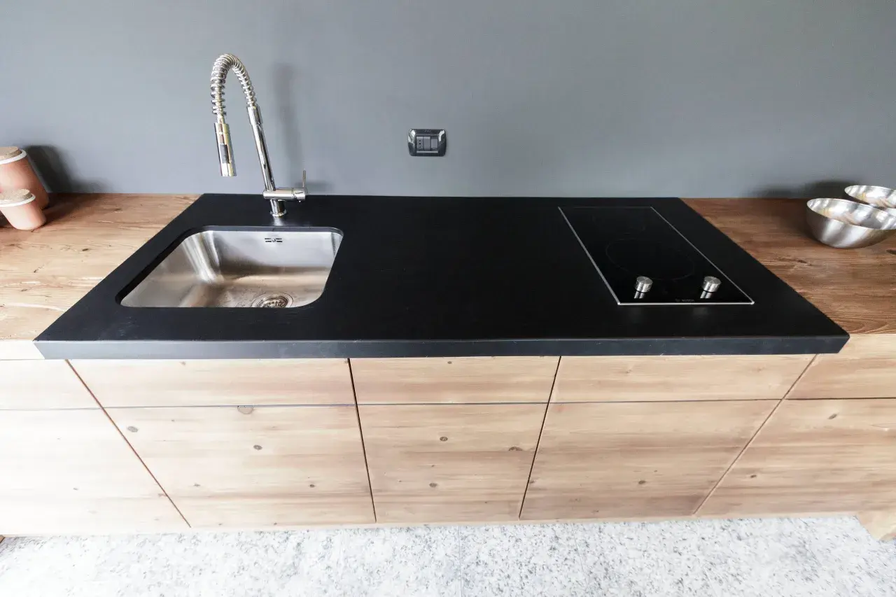 Mobile lavello cucina fai da te con piano in pietra nera, piano cottura a induzione e rubinetto cromato.