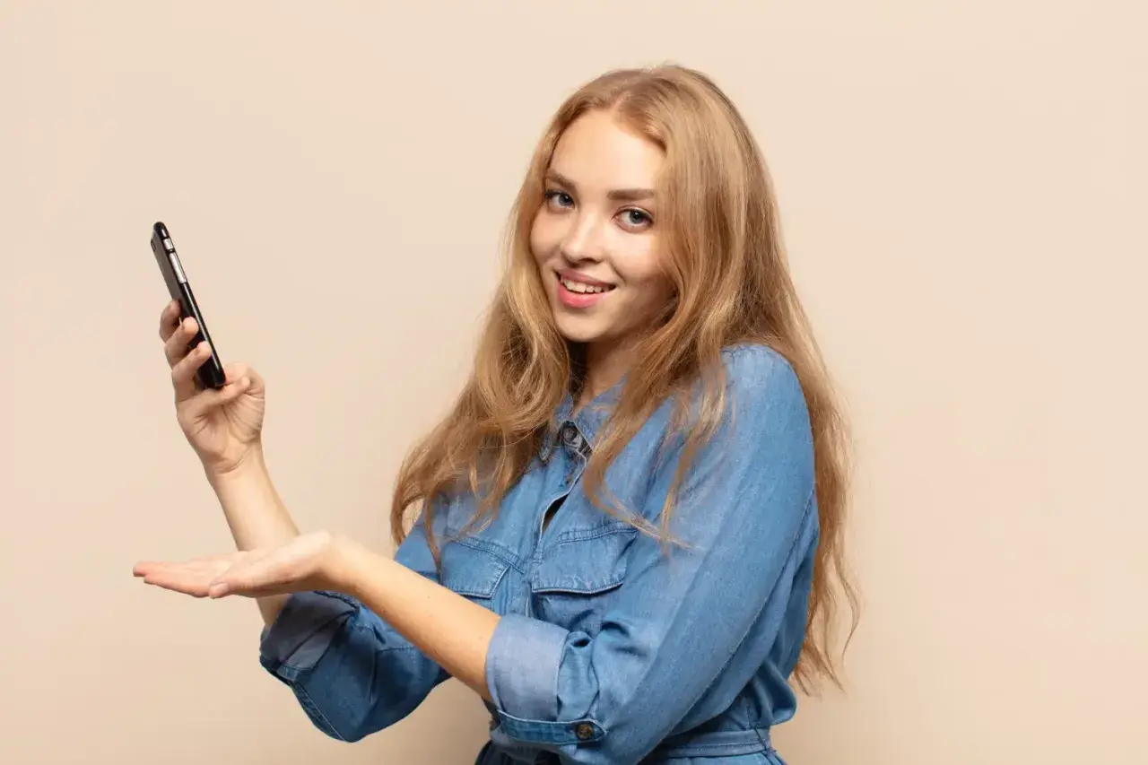 Uśmiechnięta blondynka trzyma telefon, prezentując etykietę cyfrową InPost.