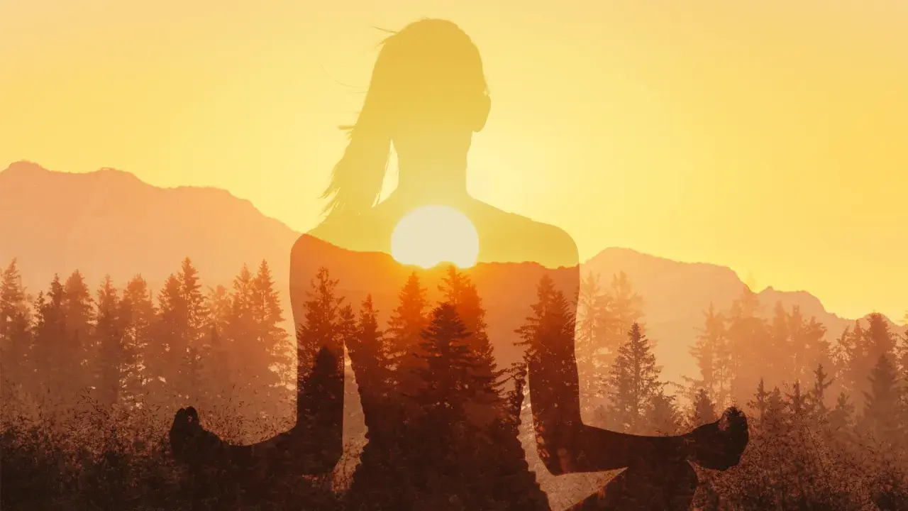 Silhouette di donna in meditazione con tramonto e foreste. Un'immagine che ispira a come ridurre lo stress con la natura.