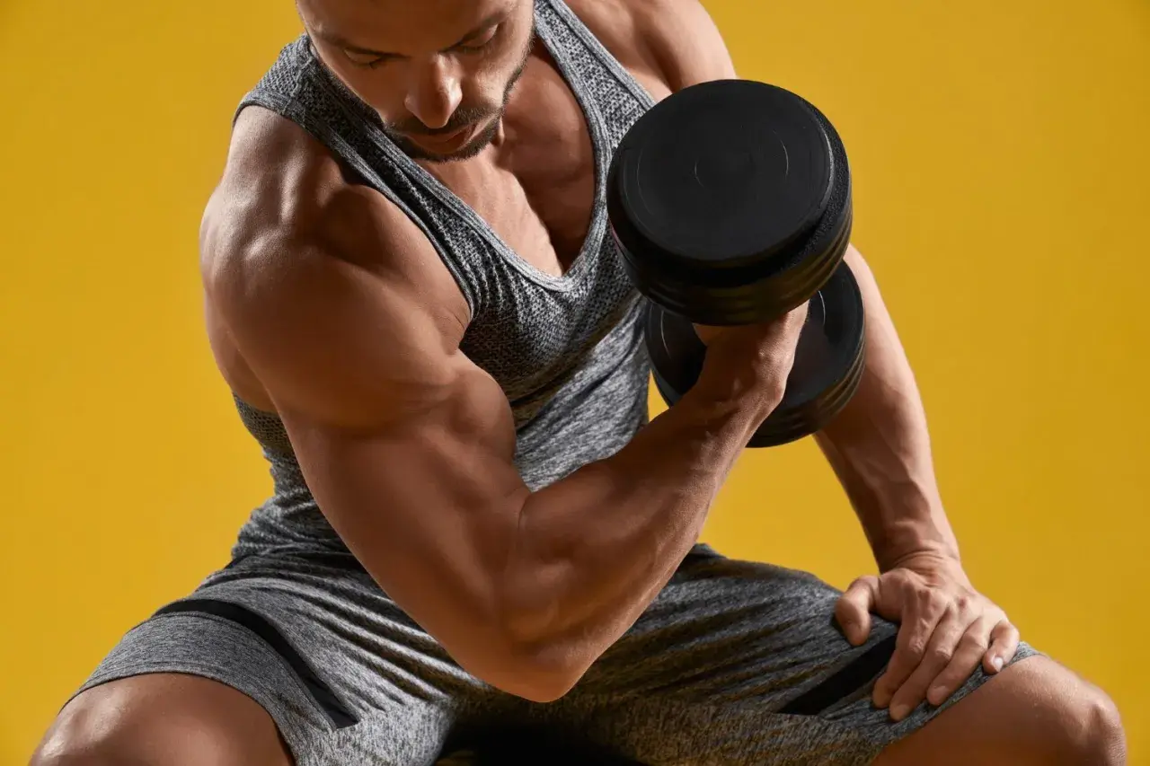 Mężczyzna ćwiczy biceps z hantlem. Widać lekkie drżenie mięśni po treningu, oznakę wysiłku.