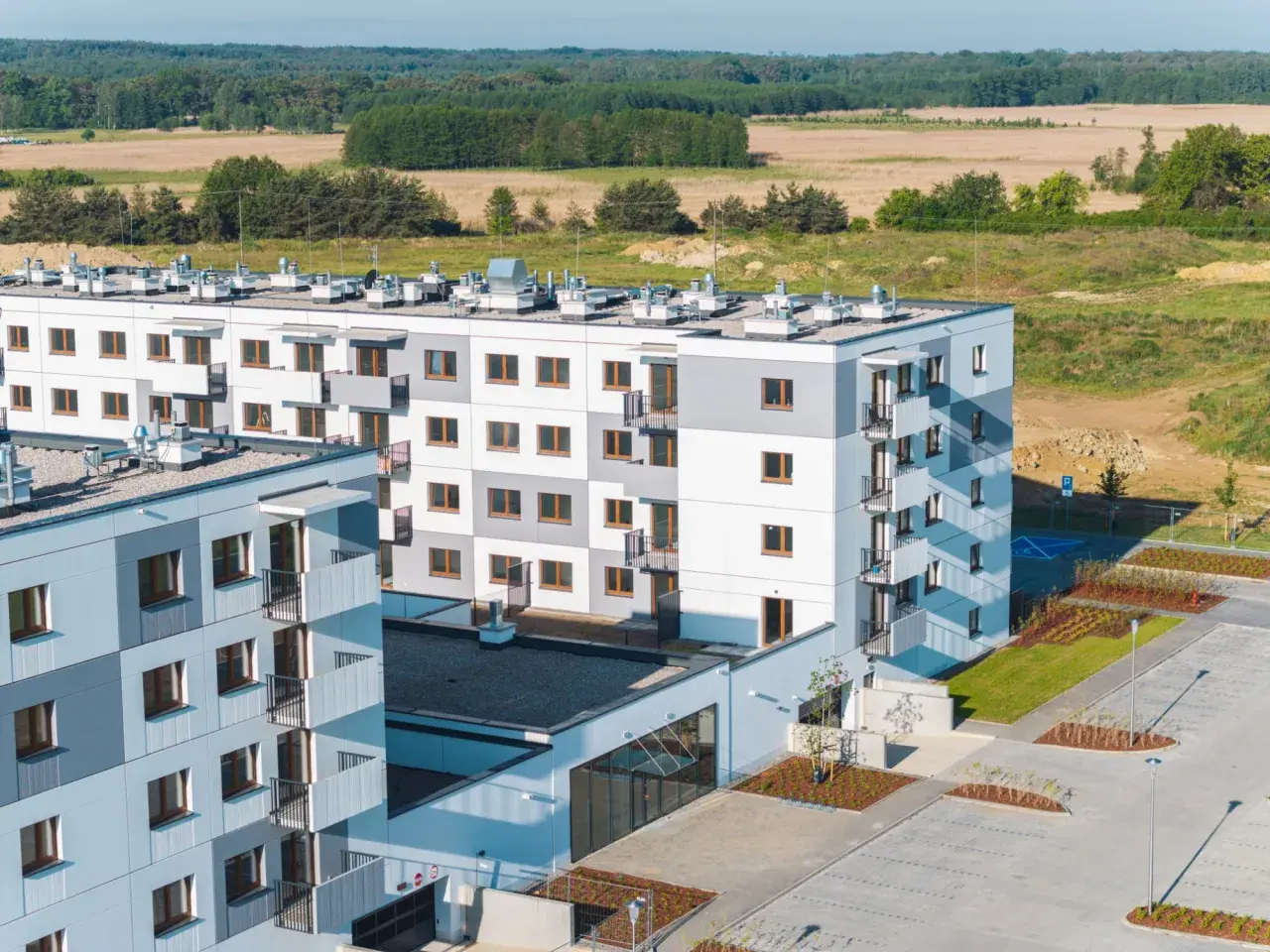 Nowa winnica Miękinia: nowoczesne bloki mieszkalne z balkonami, otoczone zielenią i parkingiem, na tle pól i lasu.
