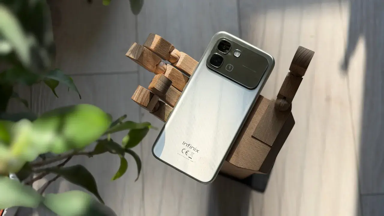 Srebrny smartfon Infinix, marka znana z innowacyjnych rozwiązań, prezentuje się na drewnianej dłoni.