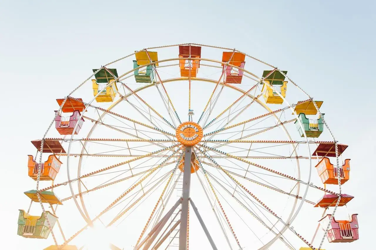 Grande roue colorée avec des nacelles jaunes, vertes, oranges et rouges sous un ciel clair.