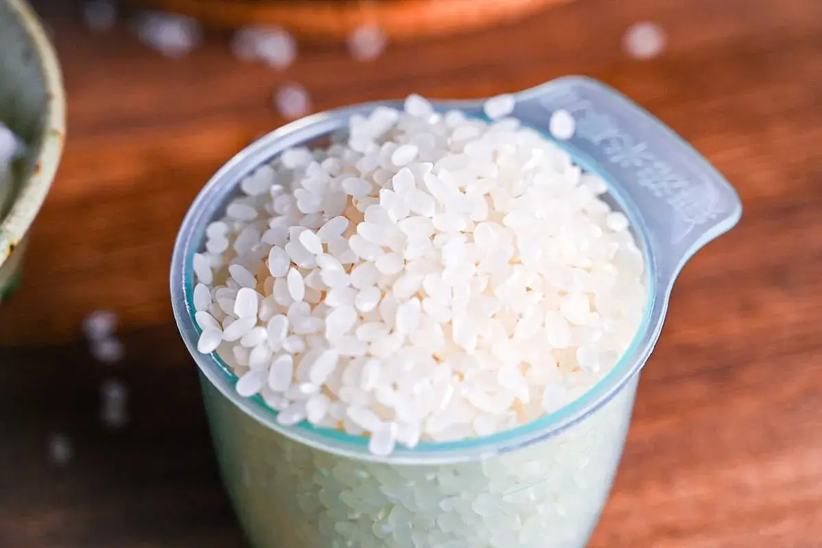 A measuring cup filled with short-grain white rice, ready for cooking Japanese rice.