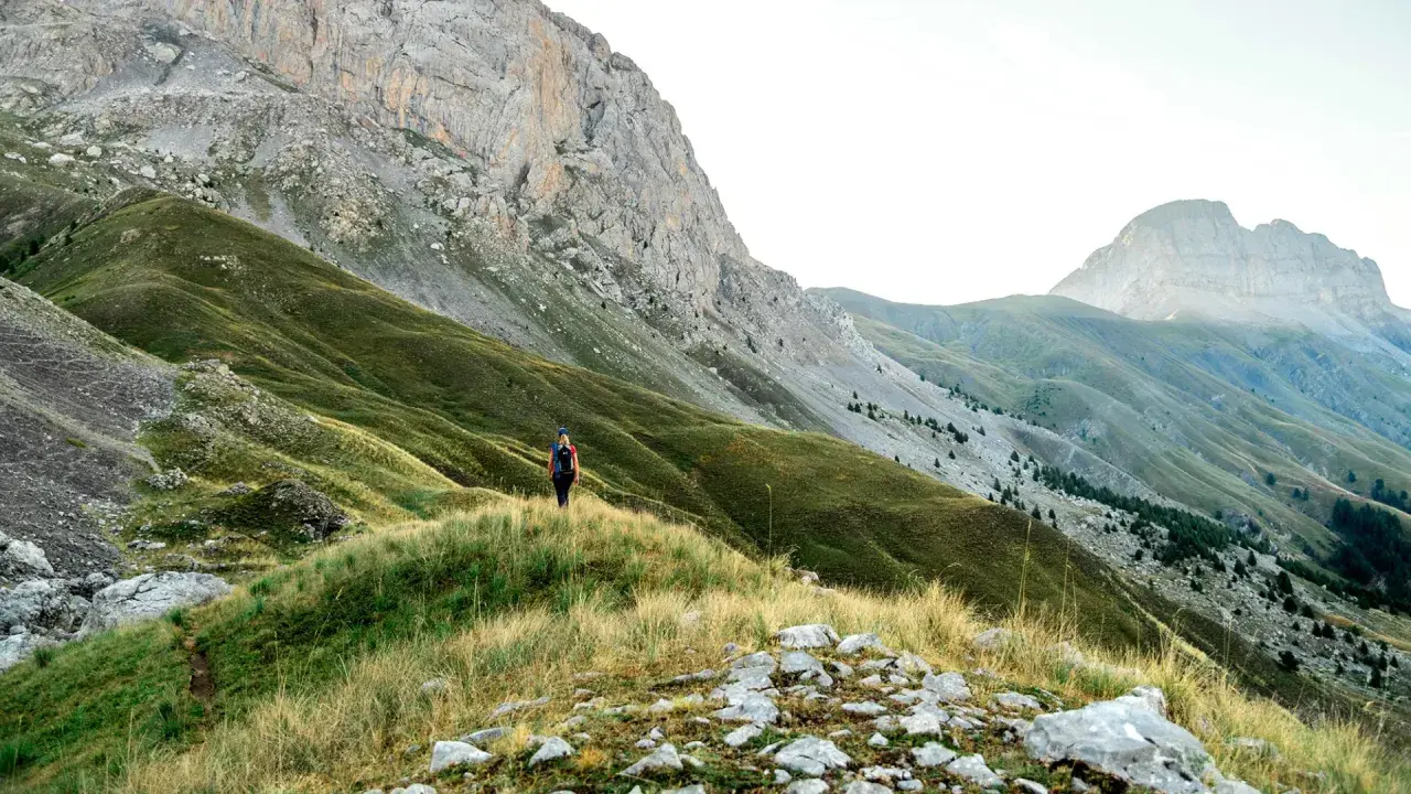 Randonneuse solitaire sur un sentier herbeux, dominant les pentes verdoyantes et les montagnes majestueuses du tour de l'Ubaye.