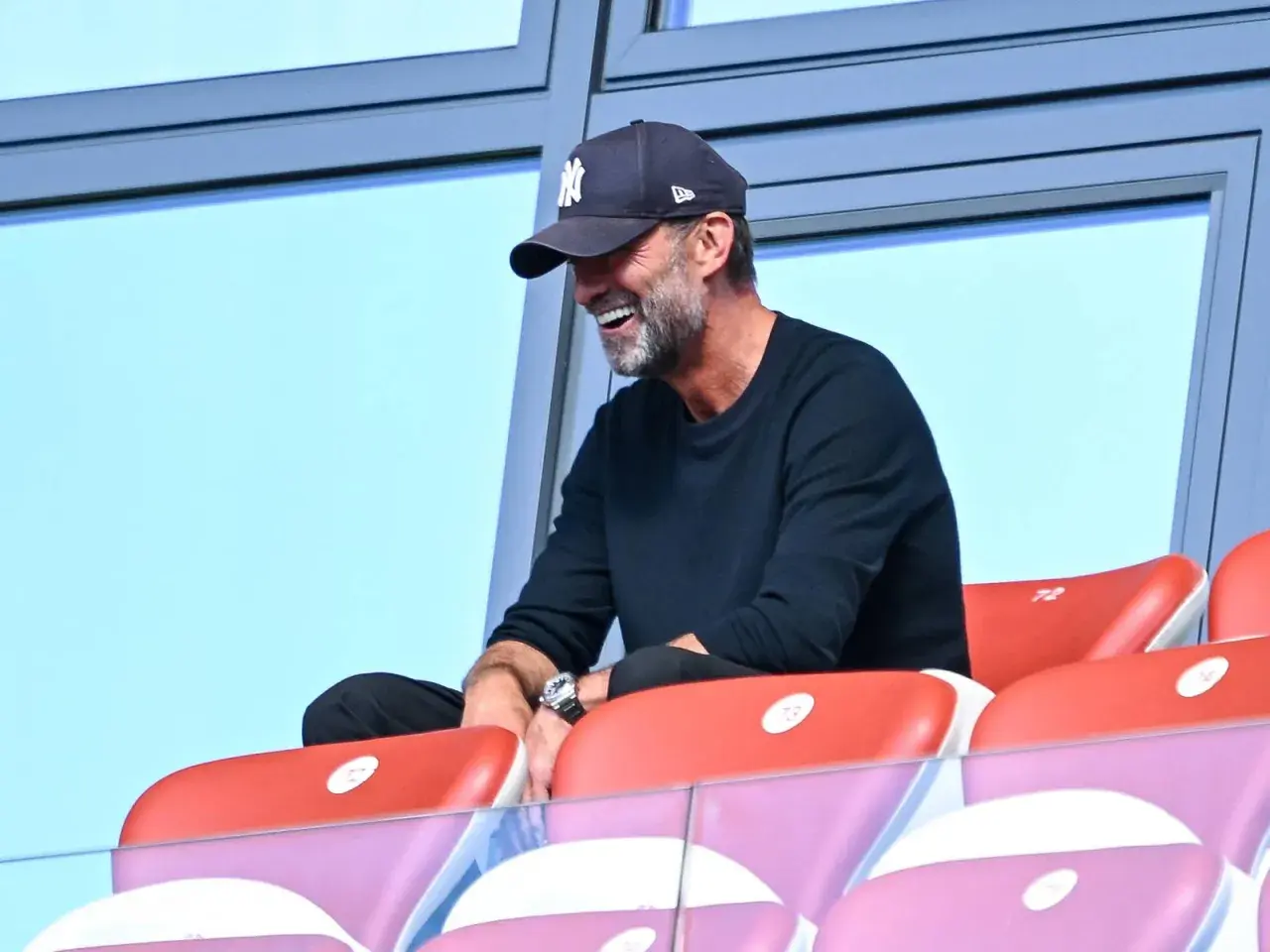 Jürgen Klopp, mit einer New York Yankees Kappe, lacht auf der Tribüne. Vielleicht beobachtet er ein Spiel des DFB.