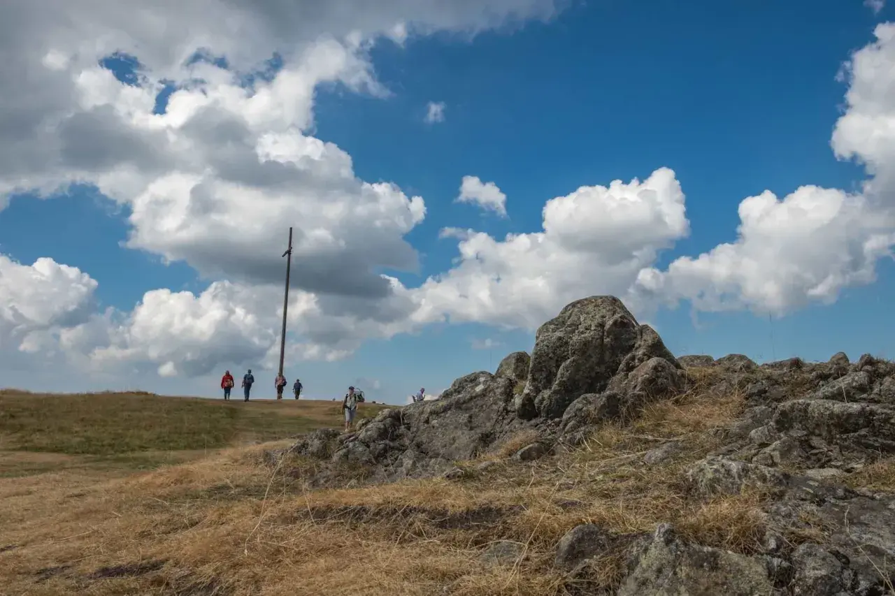 Wanderer auf dem Herzogenhorn genießen die Aussicht unter dramatischen Wolken. Ein Holzkreuz markiert den Gipfel.