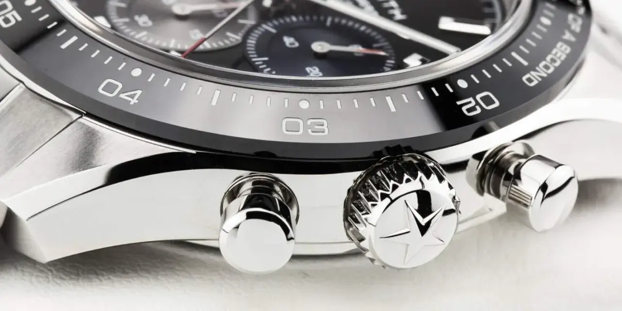 Detalle de un reloj de lujo, mostrando el bisel con números y marcas, y los pulsadores. El bisel del reloj está diseñado para cambiar la hora.