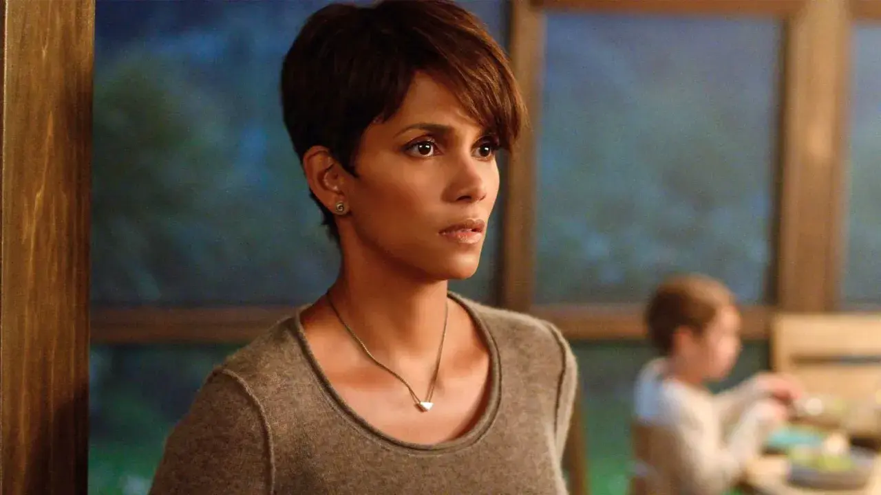 Halle Berry w filmie, zamyślona, w tle niewyraźne dziecko.