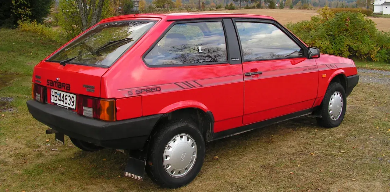 En röd Lada Samara står parkerad på en gräsmatta. Bilen har en "5 SPEED"-dekal på sidan.