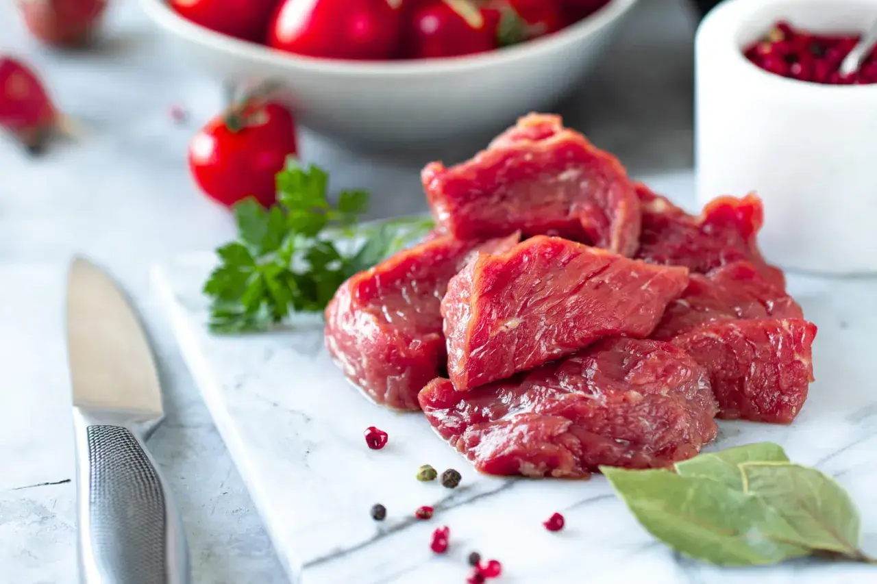 Morceaux de viande rouge crue sur une planche en marbre, avec des tomates cerises et des herbes. Question : viande hors frigo combien de temps ?