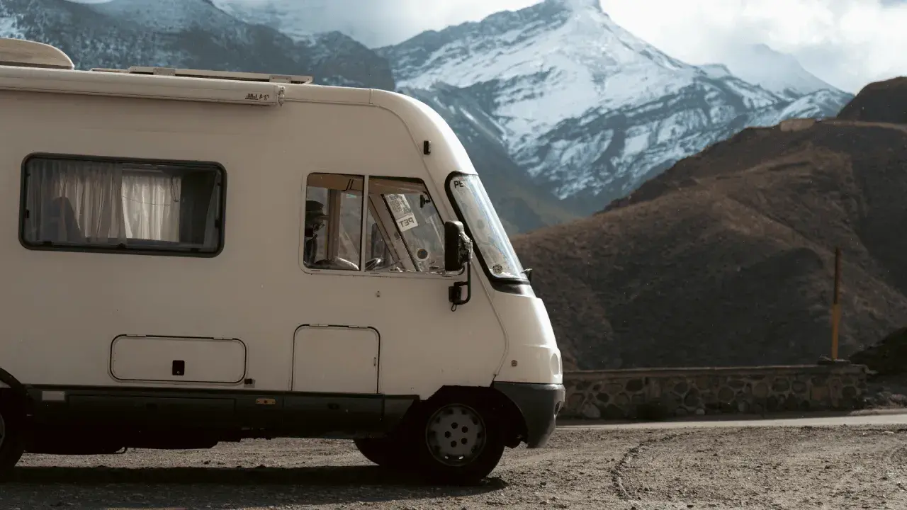Un camping-car intégral blanc stationné sur un chemin de terre, avec des montagnes enneigées en arrière-plan.