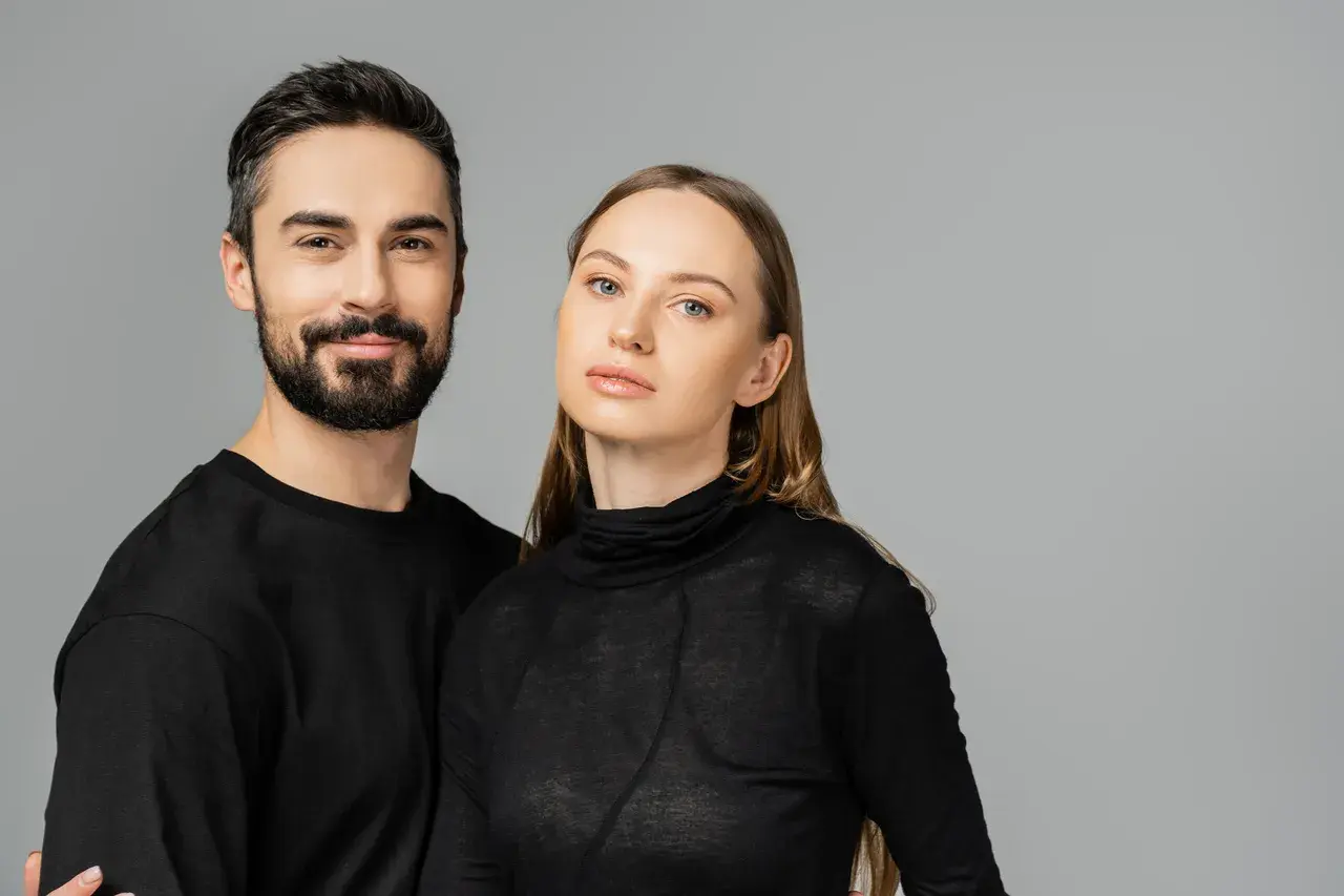 Para, która uosabia styl unisex. Mężczyzna z zarostem i kobieta o delikatnych rysach, oboje w czarnych, prostych ubraniach.