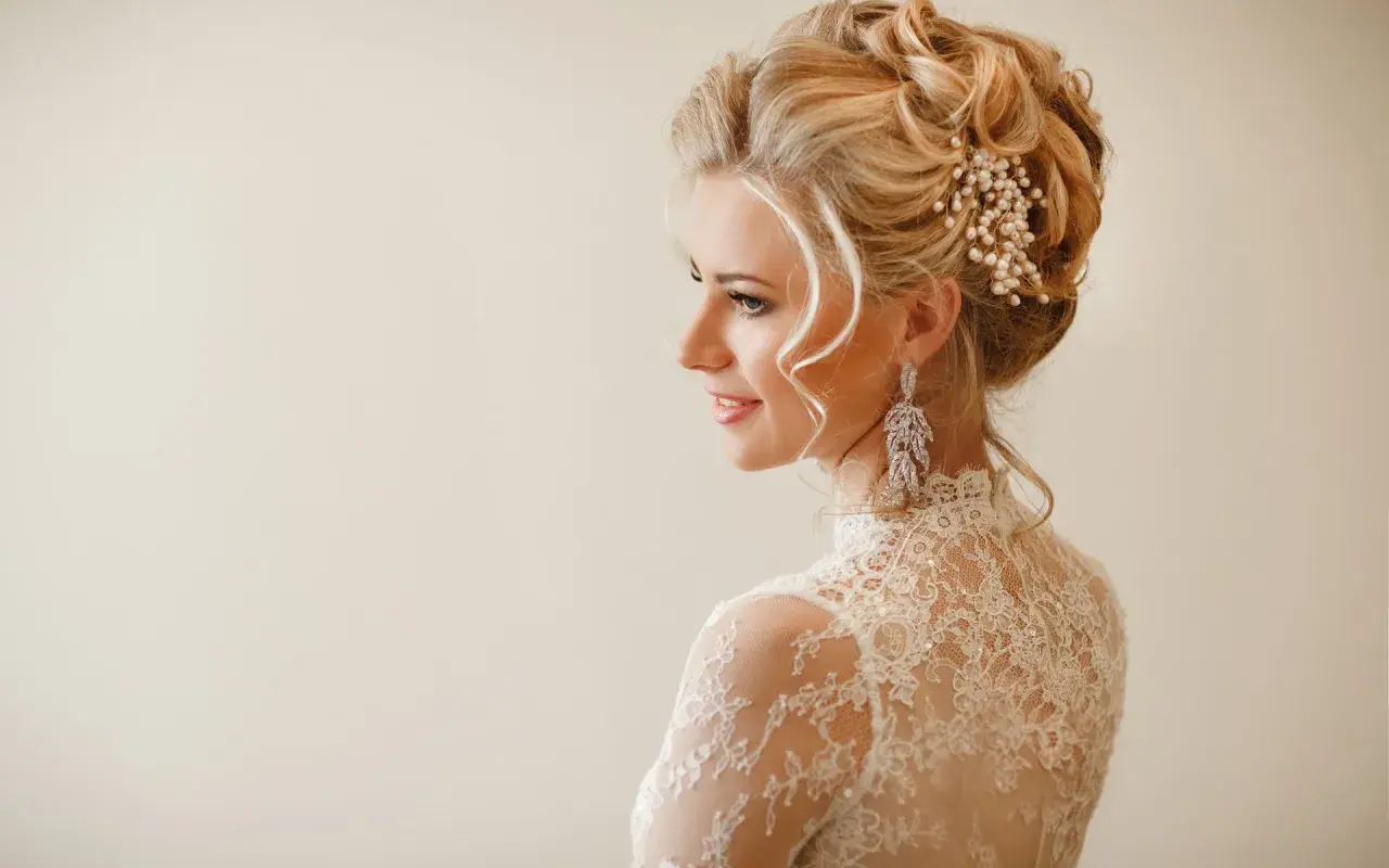 Elegancka panna młoda z upiętymi włosami ozdobionymi perłami i kryształami. Jej fryzury ślubne glamour podkreślają delikatne loki opadające na ramiona.