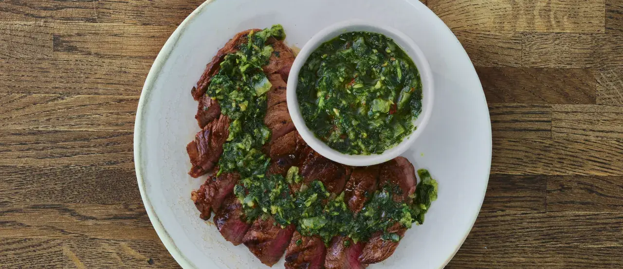 Pokrojony stek z wołowiny polany zielonym sosem chimichurri, podany na talerzu.