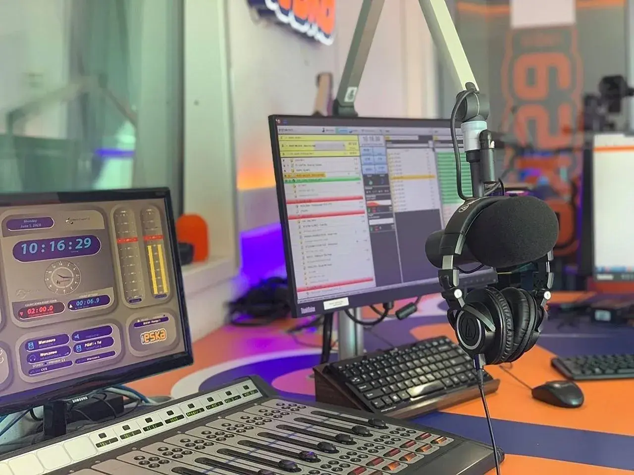 W studiu radiowym, gdzie słychać muzykę z **radio eska2 online**, wiszą słuchawki. Na monitorach widać zegar i program radiowy.
