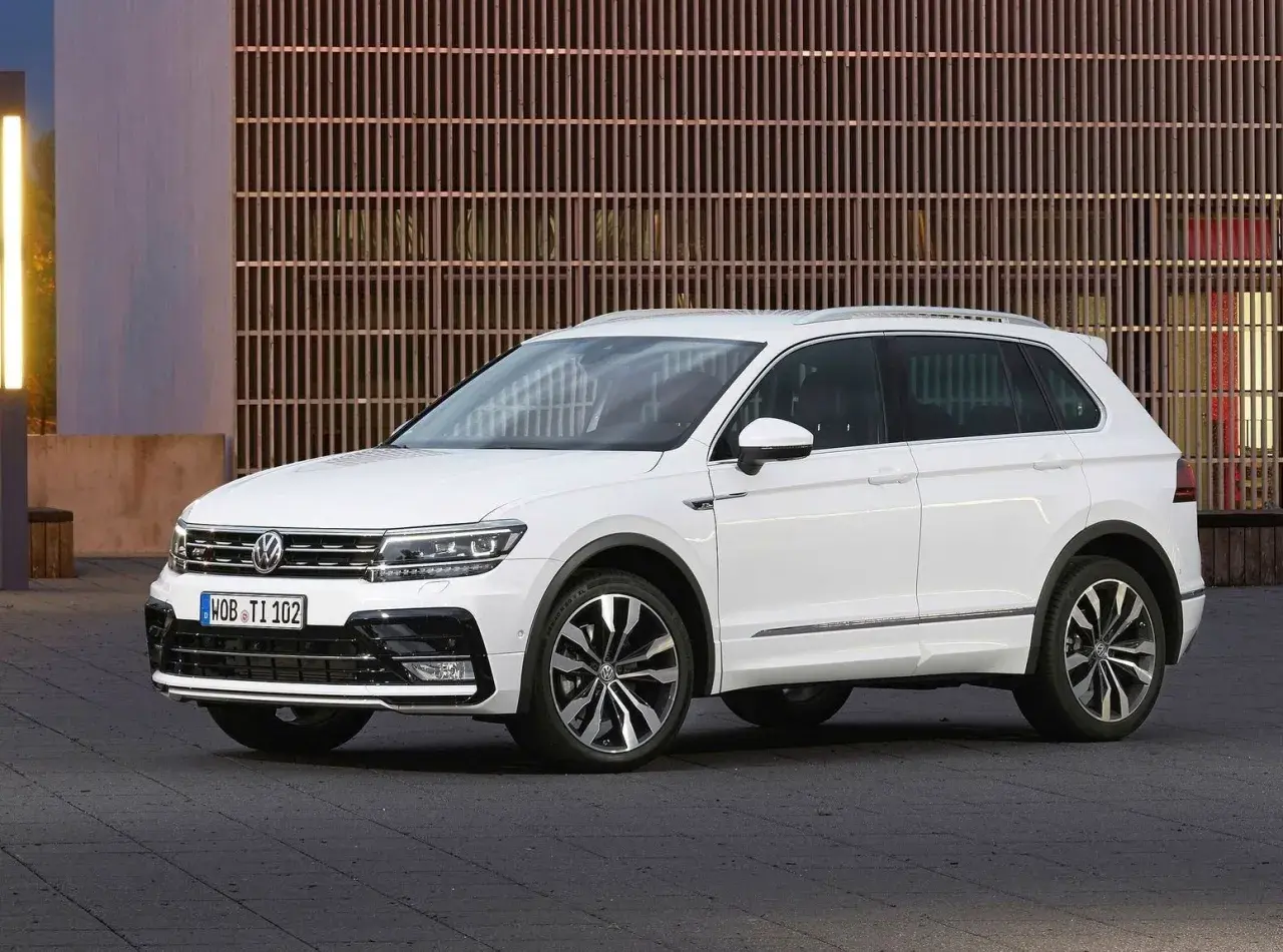 Biały Volkswagen Tiguan 2019 z eleganckimi felgami stoi przed nowoczesnym budynkiem z drewnianą fasadą.