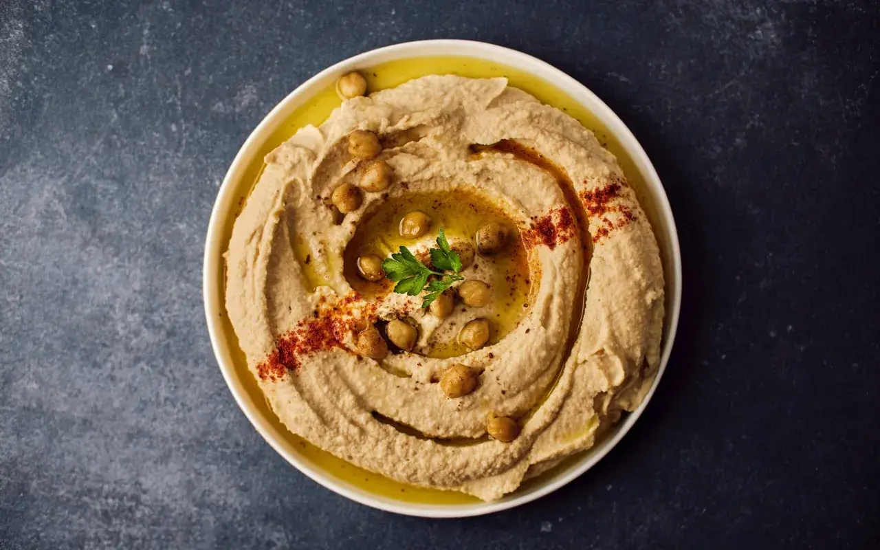 Cremoso hummus di ceci guarnito con ceci interi, paprika e prezzemolo, pronto per essere gustato.