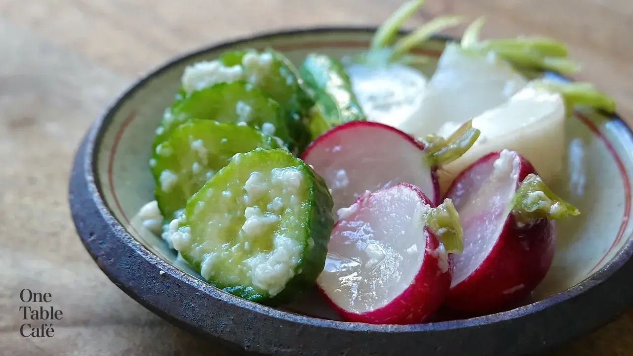 A close-up of a bowl filled with shio koji pickles. Sliced cucumbers and radishes are coated in a creamy marinade, showcasing their vibrant colors and textures.