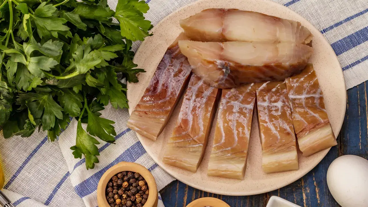 Kawałki wędzonego dorsza czarnego na talerzu, obok pęczek natki pietruszki i miseczka z pieprzem.