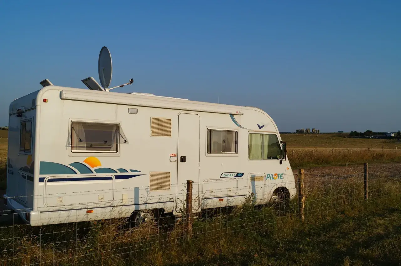 Camping-car blanc stationné dans un champ en Angleterre, avec Stonehenge à l'horizon.