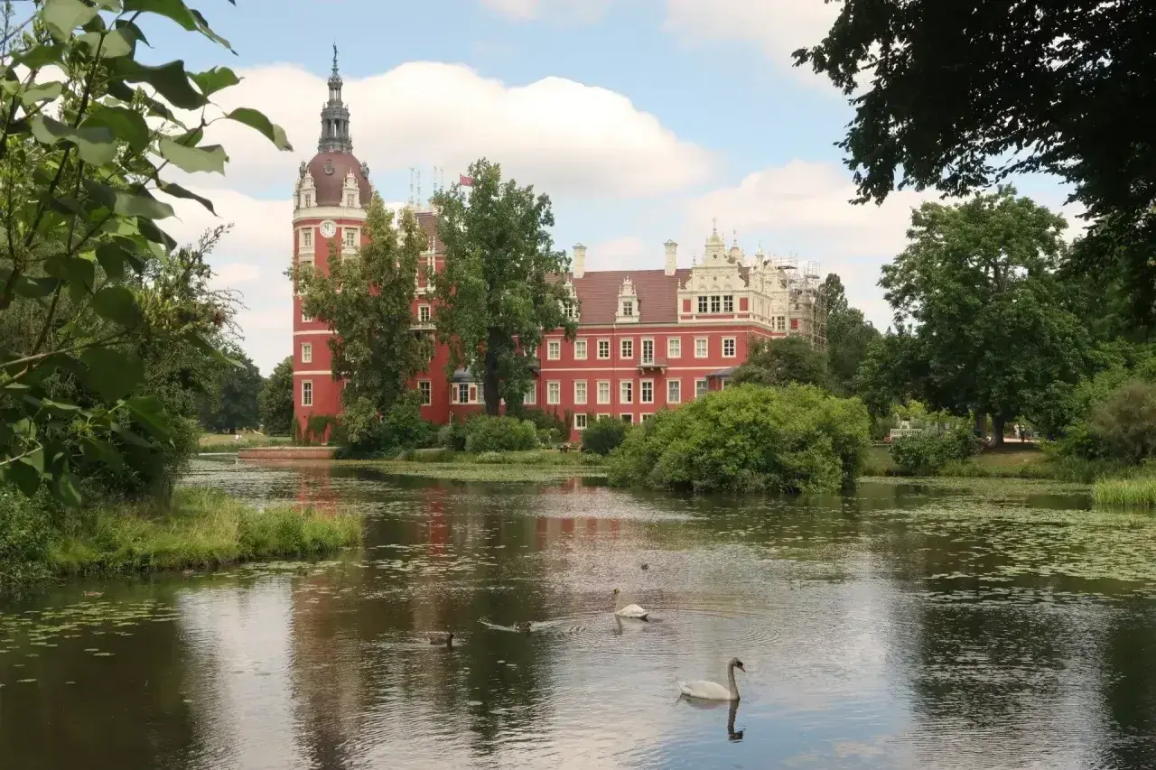 Zamek w Mużakowie zachwyca czerwienią i wieżą. Wokół jezioro z łabędziami, idealne miejsce na zwiedzanie.