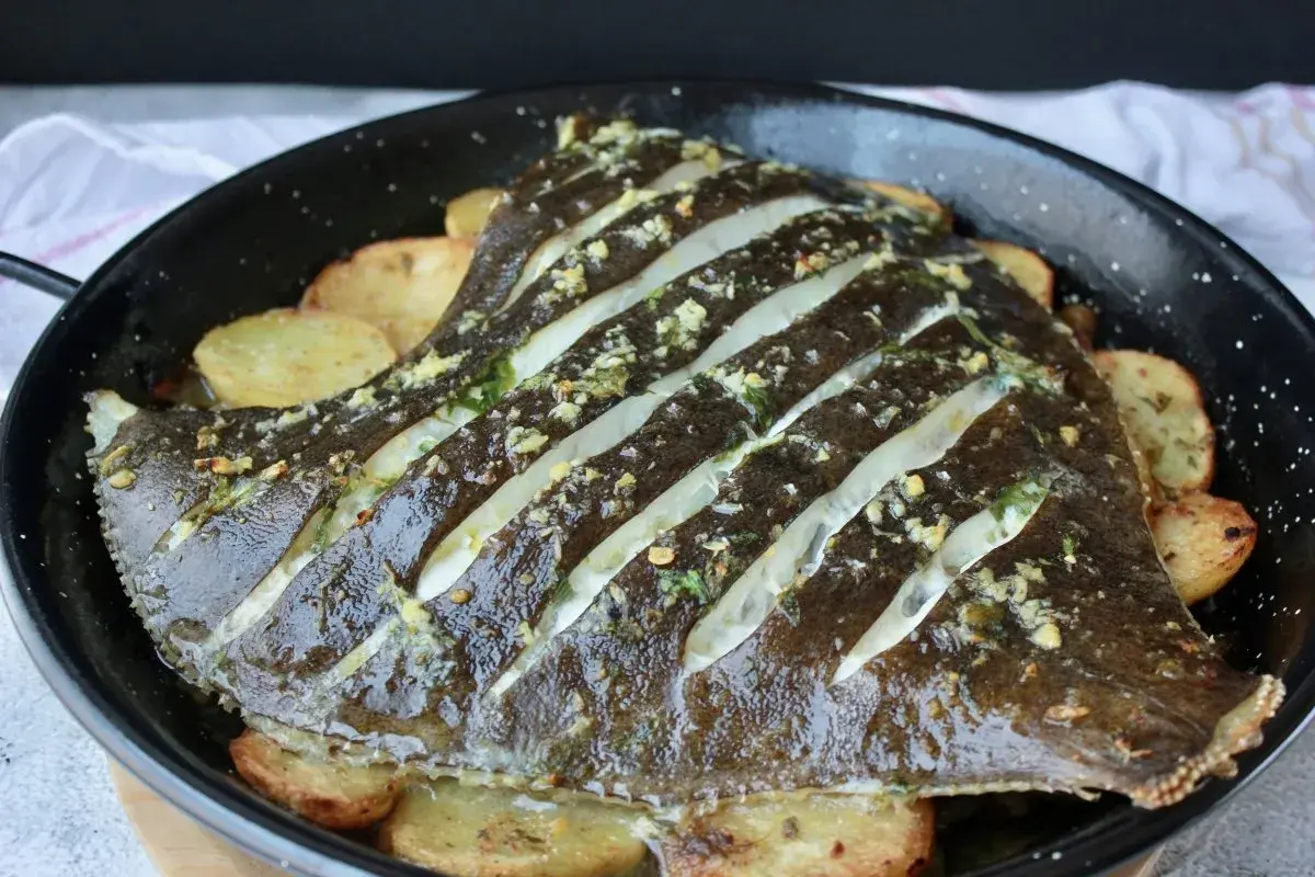 Rodaballo al horno con patatas, preparado con cortes y aderezado con hierbas y ajo.