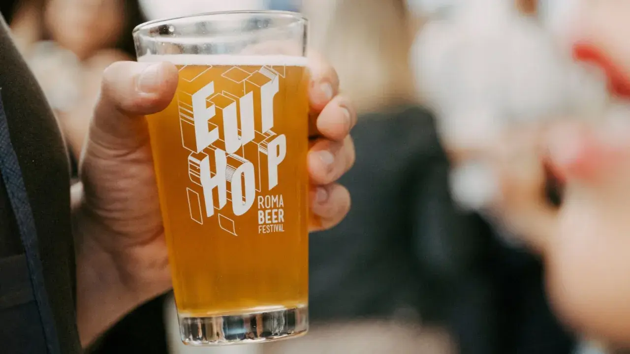 Un bicchiere di birra dorata con il logo "Eur Hop Roma Beer Festival" tenuto in mano.
