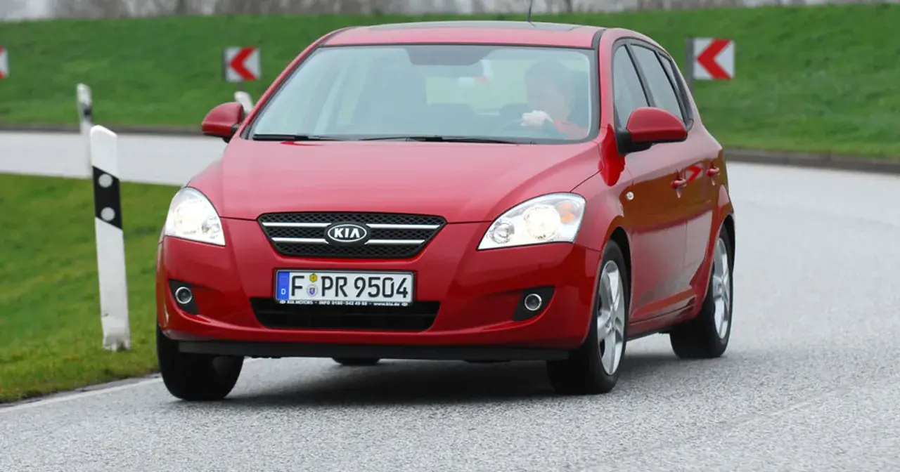 Czerwony Kia Ceed 1.6 CRDi na drodze, z kierowcą za kierownicą.