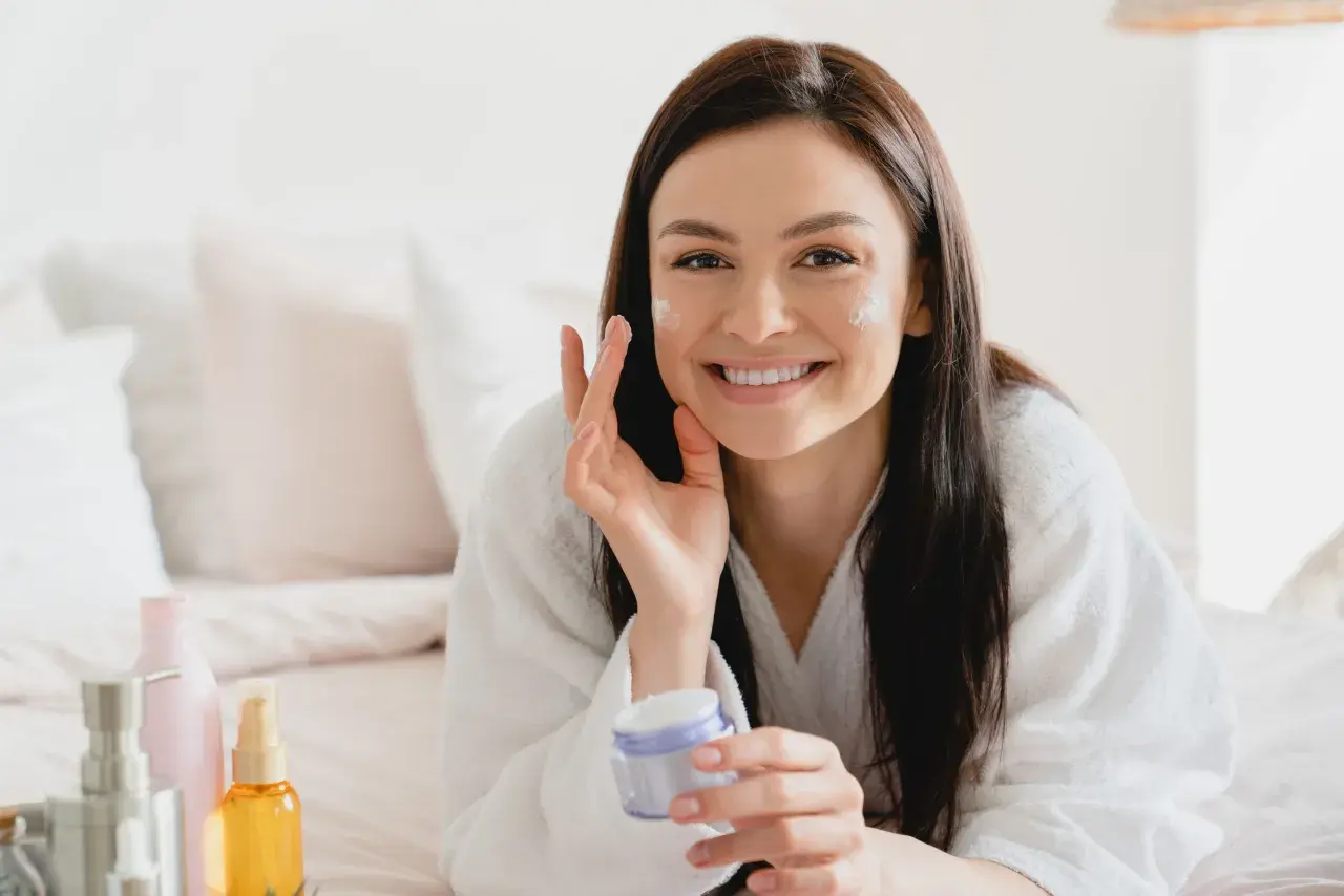 Donna sorridente applica crema viso, scoprendo i benefici di un siero probiotico per una pelle sana e luminosa.
