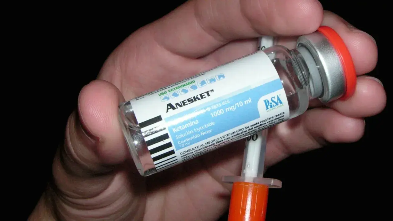 Mano che tiene una fiala di Anesket (ketamina) con siringa, suggerendo potenziali ketamina effetti positivi in contesti medici.