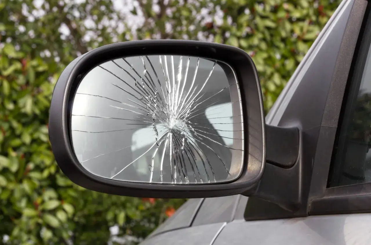 Specchietto rotto dell'auto, con il vetro frantumato in mille schegge che riflettono la luce.