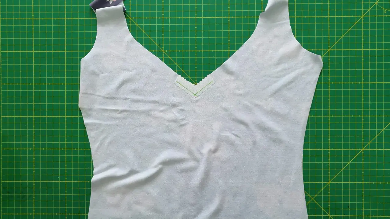 A light blue garment with a deep v neck neckline, trimmed with a delicate zigzag stitch, lies on a green cutting mat.