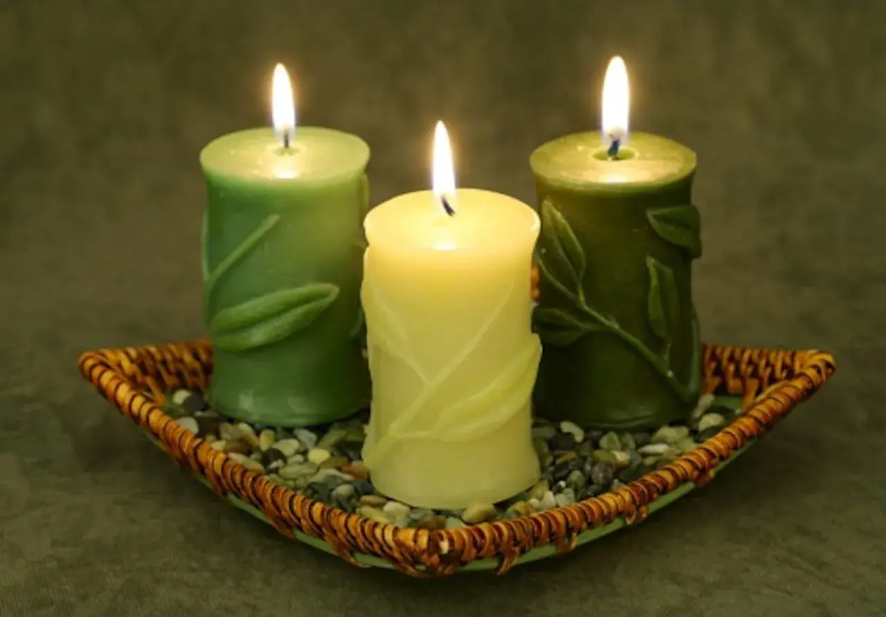 Tres velas verdes encendidas en un plato de mimbre con piedras. Encender velas en casa es malo, pero estas lucen tranquilas.