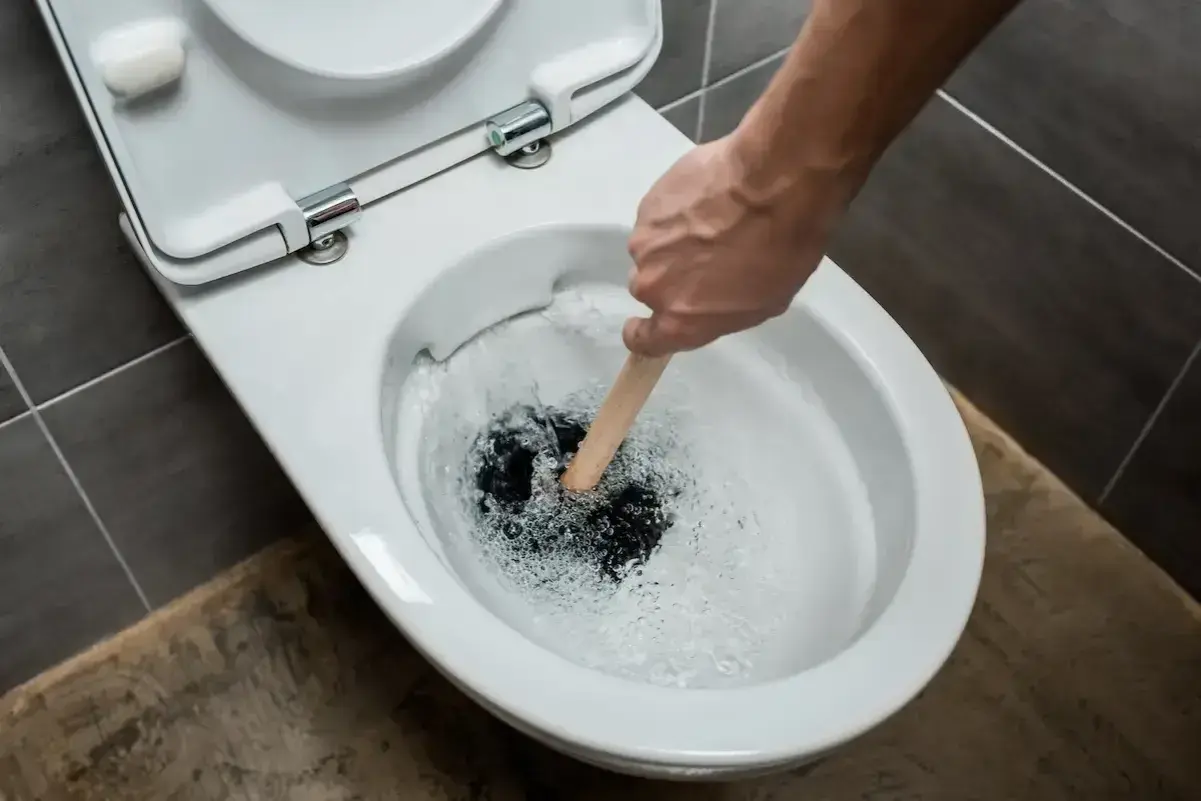 Hand plunges a toilet that is verstopft immer wieder. Water splashes around the plunger.