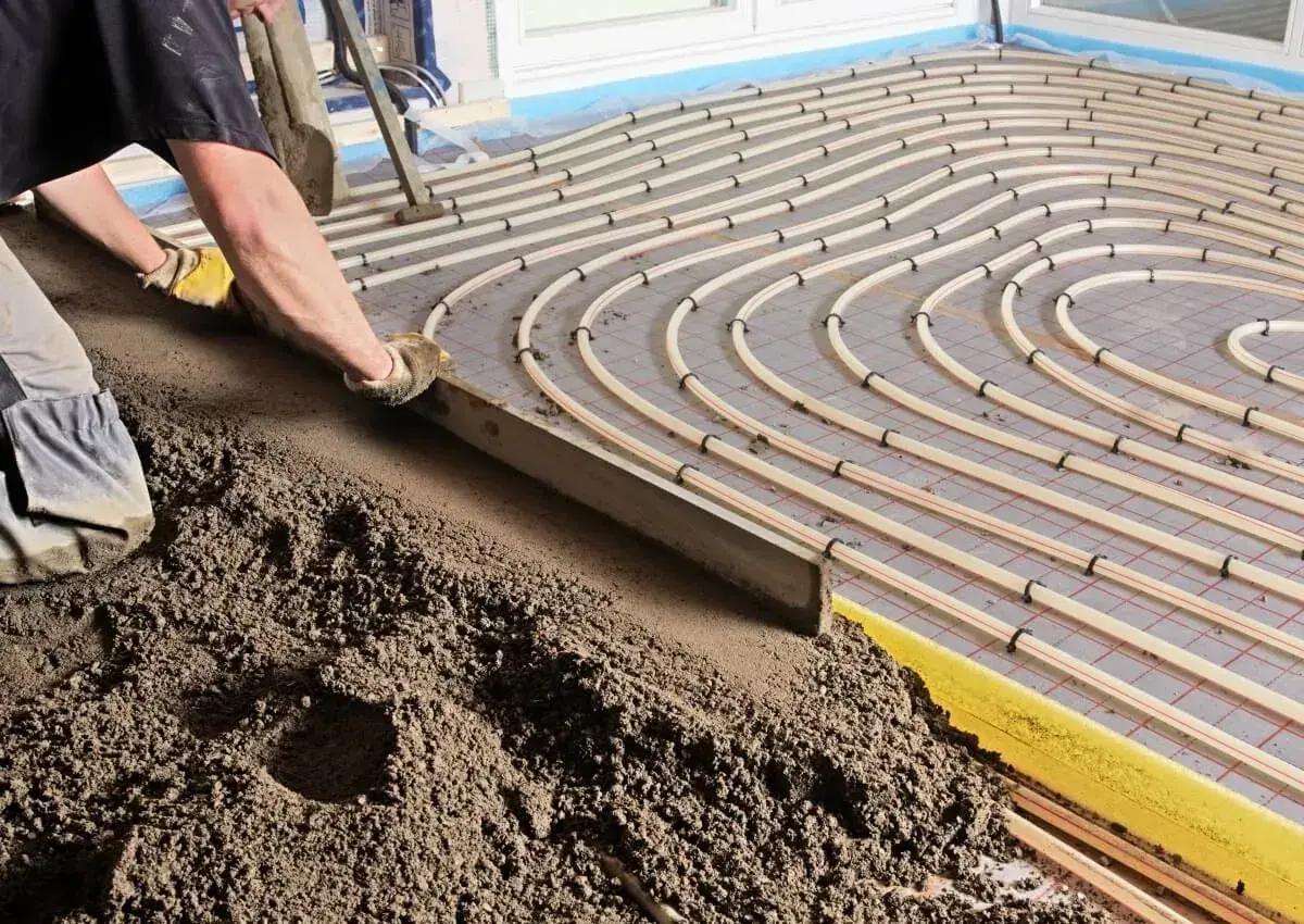 Arbeiter verlegt Estrich auf Fußbodenheizung, die den Normen nach DIN EN 13813 entspricht.