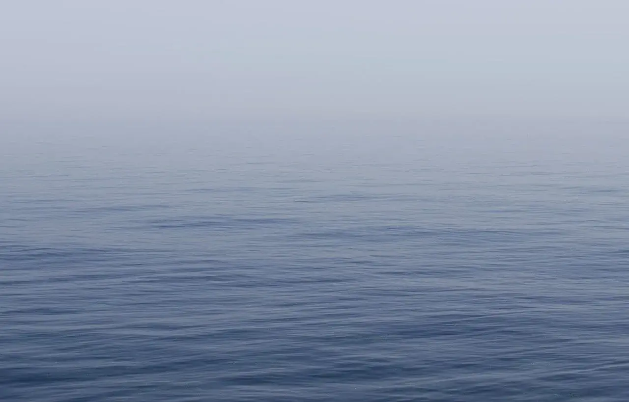 Un mar azul y tranquilo, con una bruma suave que difumina el horizonte. Un lugar perfecto para soñar con el mar azul y tranquilo.