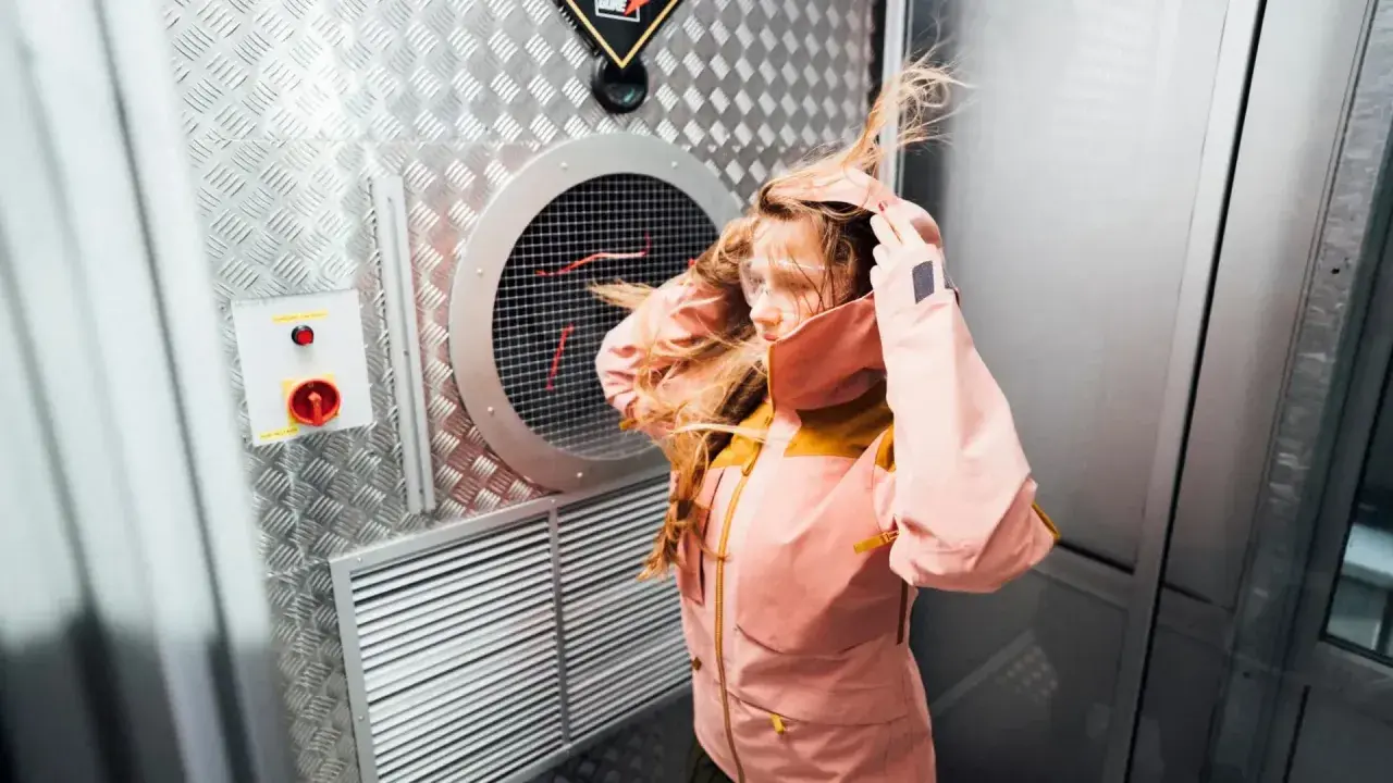 Dziewczyna w kurtce z materiału Gore-Tex co to jest, testuje jej odporność na wiatr w specjalnej komorze.