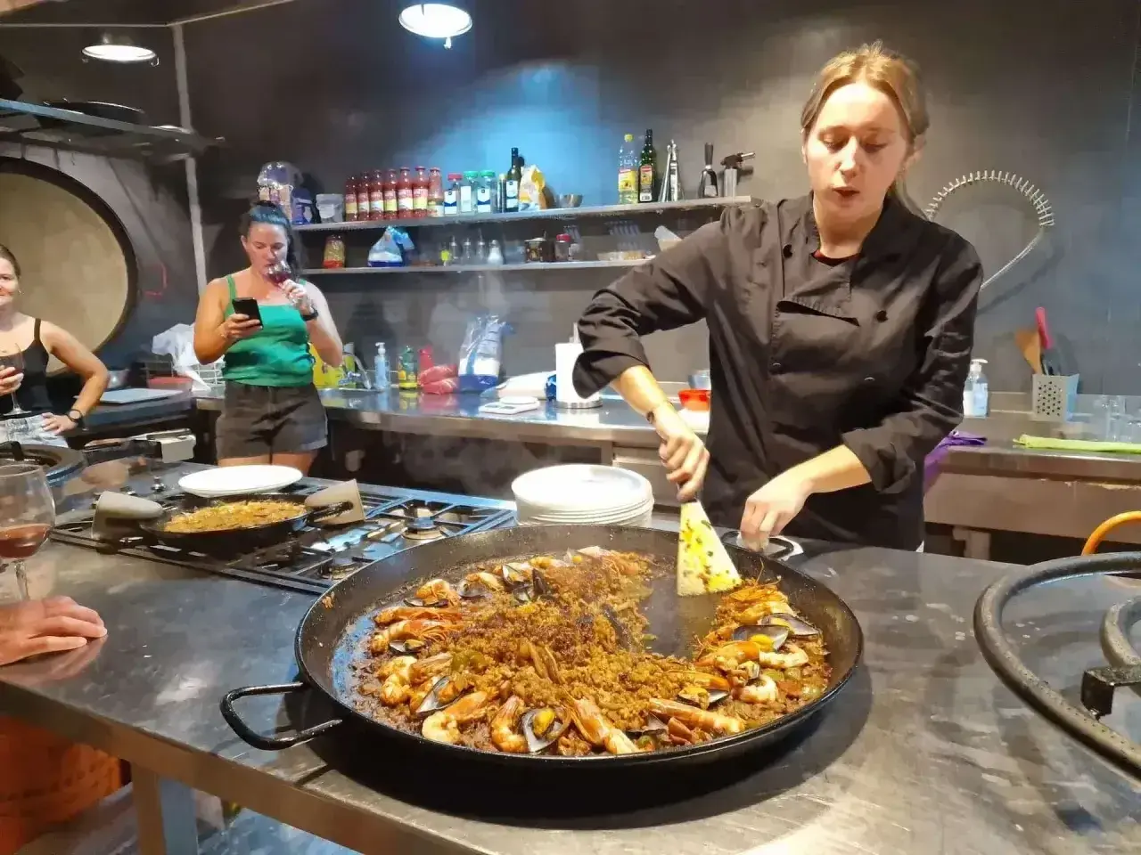 Kobieta w czarnym fartuchu przygotowuje na kuchence ogromną patelnię z owocami morza i ryżem. To musi być najlepsza paella w Barcelonie!