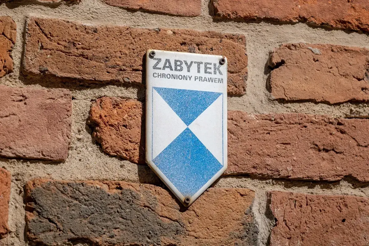 Tabliczka "Zabytek chroniony prawem" na ceglanej ścianie. Może być potrzebna do wypełnienia wzoru wniosku o wykreślenie z gminnej ewidencji zabytków.